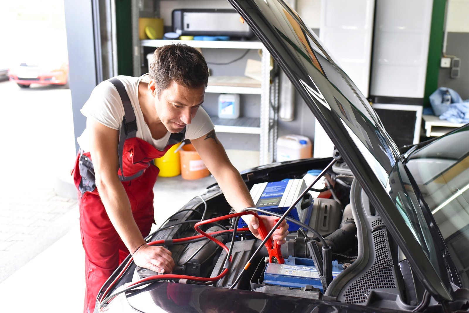 Car mechanic working in repair garage, reloading car battery