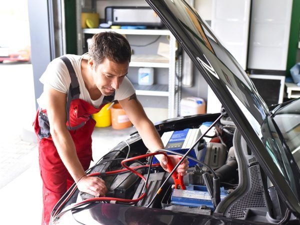 Car mechanic working in repair garage, reloading car battery
