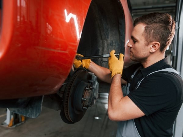 Fixing breaks. Man in uniform is working in the auto service